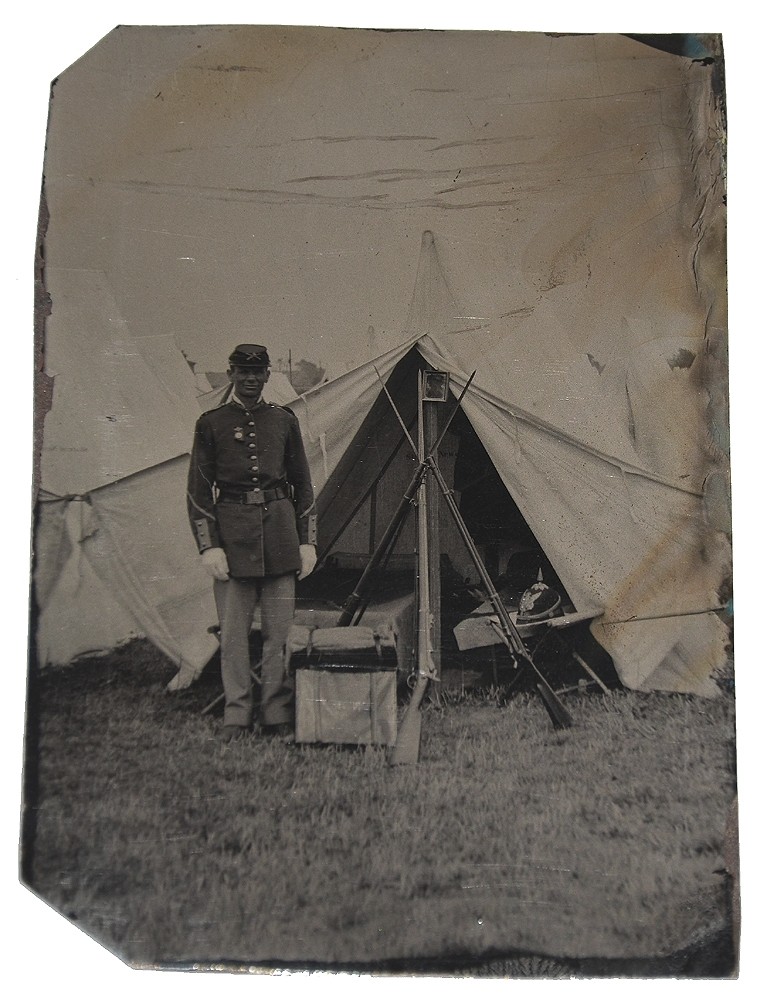 OUTDOOR 1880’S TINTYPE OF SOLDIER IN CAMP WITH STACKED MUSKETS