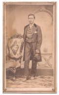 FULL STANDING VIEW OF A YOUNG MAN IN CIVILIAN CLOTHES, HOLDING A KEPI